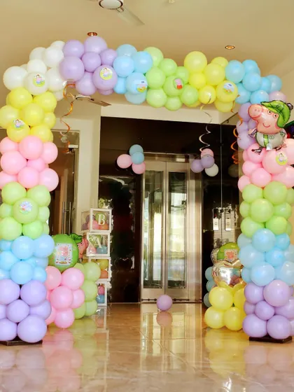 An indoor balloon arch in pastel rainbow colors for a Peppa Pig party. The Peppa and George foil balloons add the perfect finishing touch.