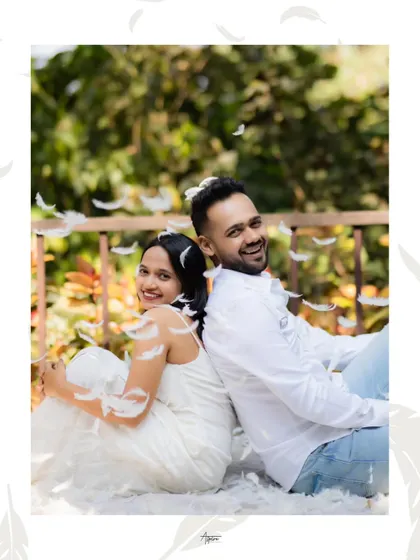A playful and joyful portrait of Nirav and Alpi sitting back-to-back amidst a shower of feathers. Their bright smiles and the whimsical atmosphere create a lighthearted and happy image.
