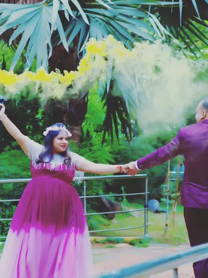 A fun maternity shoot photo using a yellow smoke bomb for a pop of color, with the couple holding hands.
