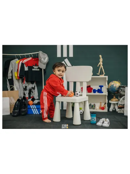 The little sports star stands by a chair in his all-red Adidas tracksuit.