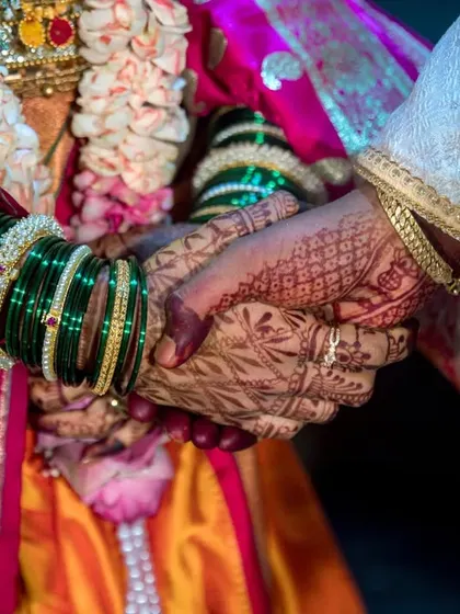 A close-up shot of the couple holding hands, symbolizing their lifelong bond. The focus is on the henna, bangles, and their intertwined fingers.
