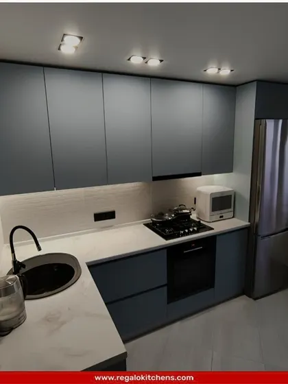 A compact and modern L-shaped kitchen in a cool blue-grey tone. The design is simple yet effective, with a round black sink and integrated appliances making it a perfect fit for a smaller apartment or home.