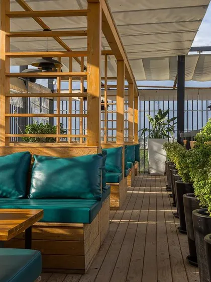 For this rooftop bar, we designed comfortable cabana-style seating with wooden frames and plush teal cushions. The retractable fabric roof provides shade during the day, creating a perfect spot for relaxed conversations.