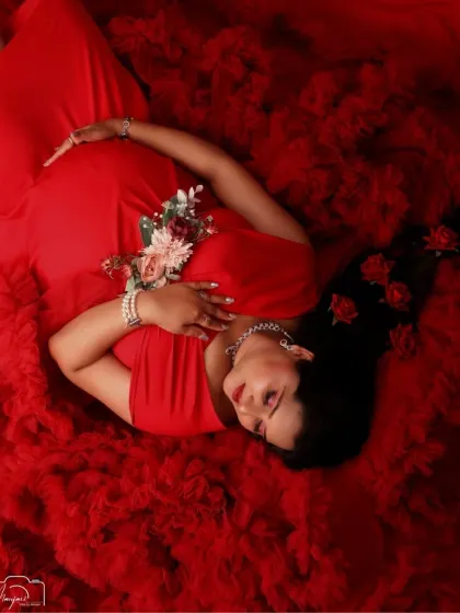 Lost in a dream of red. This peaceful sleeping pose, surrounded by the rich texture of the gown and delicate roses, creates a timeless and romantic maternity portrait.