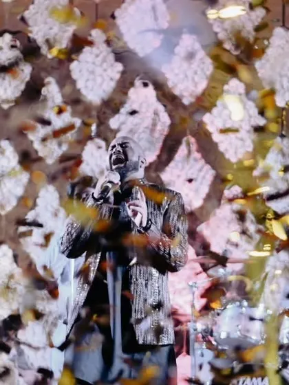 A moment of musical bliss during a Sufi night. A shower of petals rains down on the lead singer as he captivates the audience, his voice echoing through the hall against a backdrop of white floral latticework.