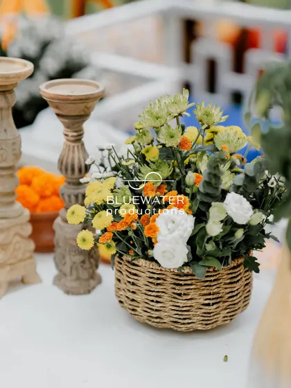 A rustic centerpiece in a woven basket, filled with a mix of yellow, white, and green chrysanthemums.