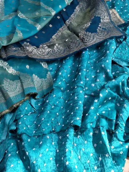 A close-up of the beautiful Banarasi Bandhej fabric in a vibrant teal color. The intricate weaving and the delicate bandhej dots create a stunning texture.