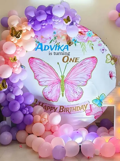 A beautiful Butterfly theme for a first birthday celebration. This design features a circular backdrop with a large butterfly graphic, a pastel balloon arch in shades of pink and purple, and a light-up number '1' for a whimsical touch.