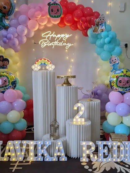 A colorful Cocomelon themed birthday party with a rainbow balloon arch, neon sign, and light-up marquee letters.