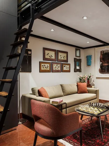 This small sitting room in the Courtyard Home features a mezzanine level accessed by a ladder, a clever solution for maximizing space. The room is filled with an eclectic mix of art and objects, creating a cozy and characterful retreat.