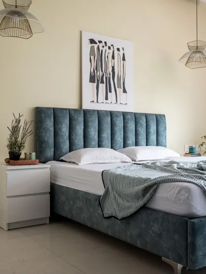 A simple yet sophisticated bedroom featuring a channel-tufted headboard in a calming blue fabric. The look is completed with minimalist white nightstands and woven pendant lights that add a touch of warmth.