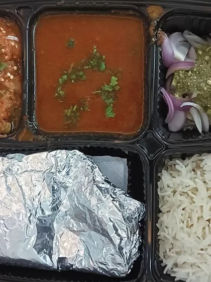 This thali features two unique dishes: black chole and baingan bharta (roasted eggplant mash). It's a rustic and authentic meal full of smoky flavors.