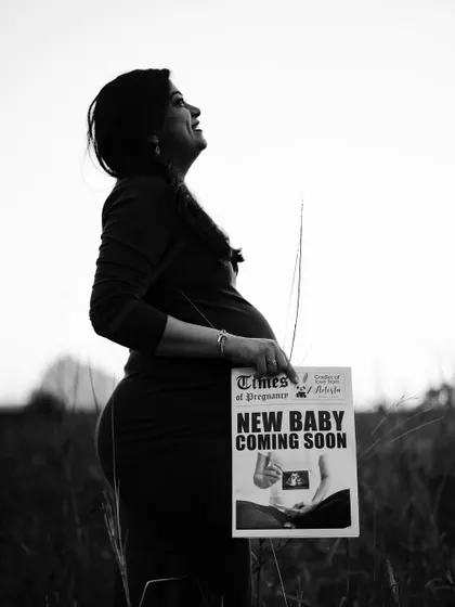 A hopeful and uplifting black and white portrait. The mom-to-be looks towards the sky, proudly holding her announcement newspaper.