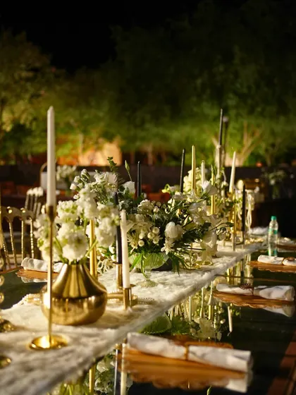 A long, mirrored table runner reflects the candlelight and white floral arrangements at the 1920s-themed Sangeet.