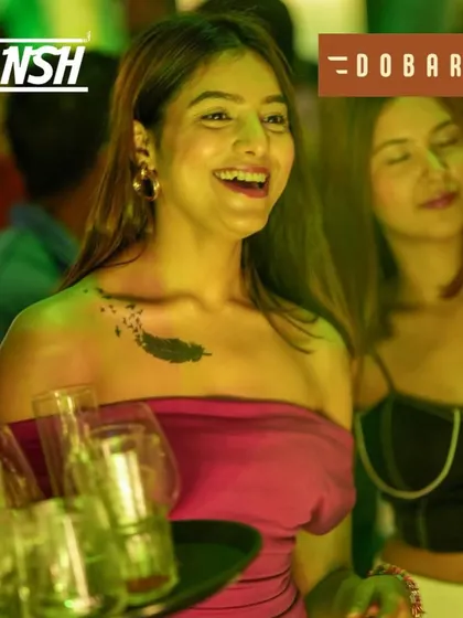 A guest with a beautiful smile, carrying drinks and enjoying the party at Dobaraa.