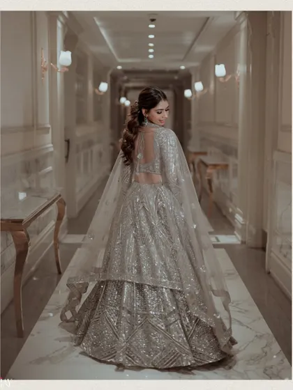 The bride walks down a luxurious corridor, her silver lehenga shimmering with every step.