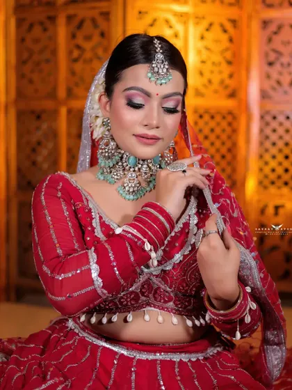 A close-up of the bride in her red and silver lehenga. Her pose, with her hand gently touching her jewellery, highlights the stunning turquoise and diamond necklace.