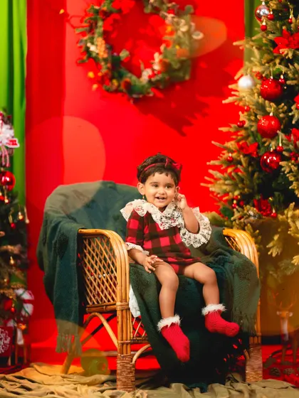 Sitting like a little queen on her chair, this toddler is all smiles in her festive Christmas outfit.