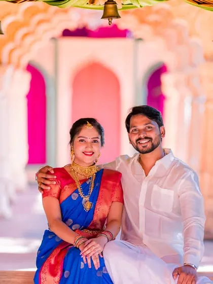 A happy couple poses on a decorated swing, surrounded by colorful drapes and flowers. Their traditional attire adds to the festive and joyful mood.