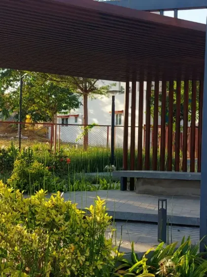 A shaded seating area or bus stop with a modern design, integrated into a park landscape. The surrounding plants soften the structure and provide a pleasant waiting environment.