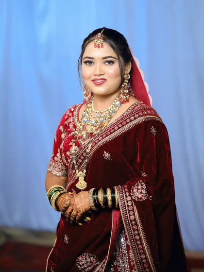 A full view of the bride in her red velvet saree. The complete look, including the hair, makeup, and draping, comes together to create a timeless and elegant bridal appearance.