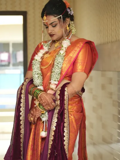 A full-length view of this bride's traditional attire. The makeup and hair were styled to perfectly complement her beautiful orange silk saree and intricate gold jewelry.
