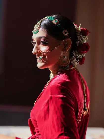 A beautiful profile shot of the bride, highlighting her elegant hair adorned with red roses and her traditional jewelry.