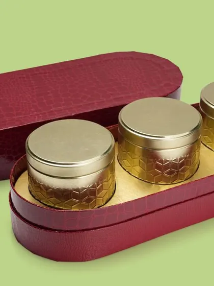 A luxurious red oval box with three golden tins inside. This shot effectively showcases a complete packaging solution for gifting.