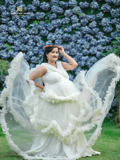 This is a duplicate of image 19. A full-length view of our popular white ruffled gown against a beautiful wall of blue flowers, perfect for creating dramatic and angelic maternity portraits.