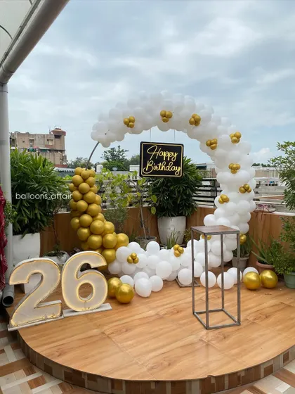 A wide view of the elegant 26th birthday terrace decoration, showing the full semi-circular balloon arch in white and gold.