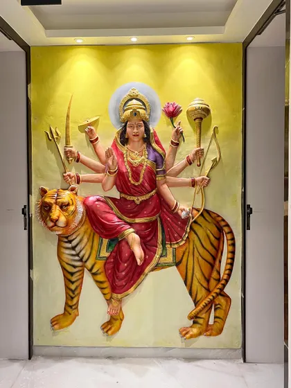 The fully installed and painted Maa Durga fiber mural, creating a powerful spiritual centerpiece between two doorways. The vibrant colors and golden accents bring the entire sculpture to life.
