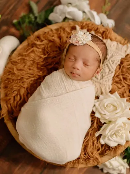 All snuggled up and dreaming sweet dreams. This image showcases a classic newborn wrap, keeping the baby secure and serene amidst soft floral props.