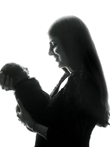 A beautiful silhouette of a mother holding her newborn. This artistic technique uses backlighting to create a dramatic and timeless image that focuses on the iconic shape of the mother and child bond.