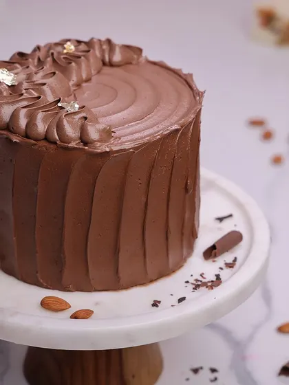 We create the ultimate indulgence with our chocolate almond cake. This rich, multi-layered chocolate cake is frosted with a silky chocolate buttercream and adorned with delicate gold leaf, offering a luxurious and classic dessert for Mother's Day.