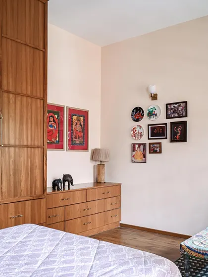 A tranquil parent's bedroom with blush-hued walls, Sabyasachi wallpaper, and a gallery wall of family photos.