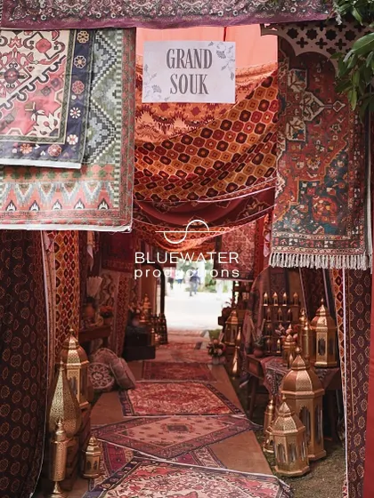 The entrance to a Dubai-inspired 'Grand Souk' Mehendi, where guests are welcomed through a tunnel of layered carpets, rich textiles, and glowing brass lanterns.
