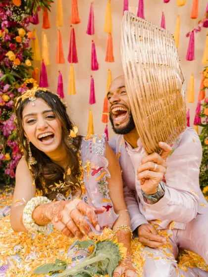 The couple shares a huge laugh while playing with a traditional hand fan amidst the flower petals. This photo is full of life, energy, and their infectious happiness.