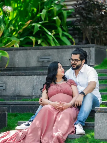 A couple sharing a quiet moment, seated on stone steps in a park. This image captures the simple, relaxed intimacy of their pregnancy journey.