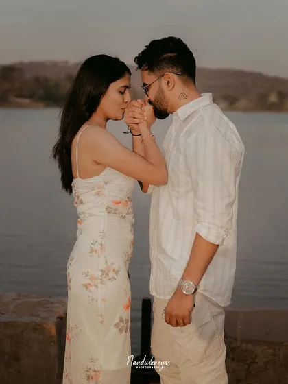 A gentle and intimate moment where the groom kisses the bride's hand as they stand by the water at sunset.