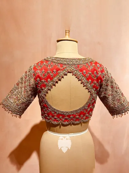 The back of a rich red raw silk blouse, featuring a distinctive checks pattern brought to life with katdana, zari, and sequins.