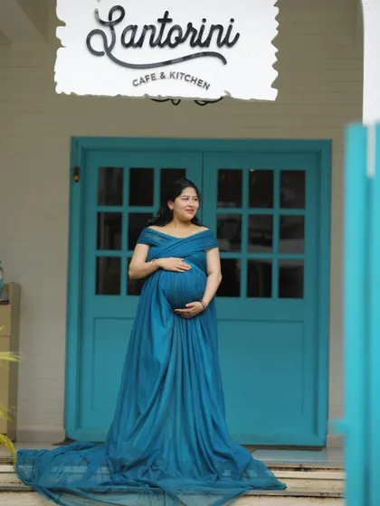 A beautiful solo portrait in our teal maternity gown. The off-shoulder design and long train create an elegant silhouette against the iconic blue and white background.