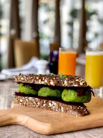 A healthy falafel sandwich in a multigrain bread. The shot is taken on a rustic wooden board, giving it a wholesome, organic feel perfect for a health-conscious cafe.