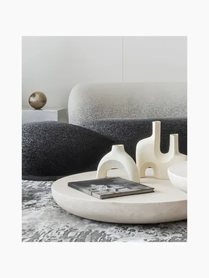 A close-up of the circular stone coffee table, adorned with minimalist white ceramic sculptures. The textures of the boucle sofa and the abstract grey rug create a rich, tactile experience, showcasing our love for layering materials.