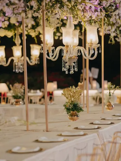 A closer view of a luxurious tablescape, with vintage-style chandeliers hanging above the table. The warm light and floral decor create an intimate and opulent dining experience.