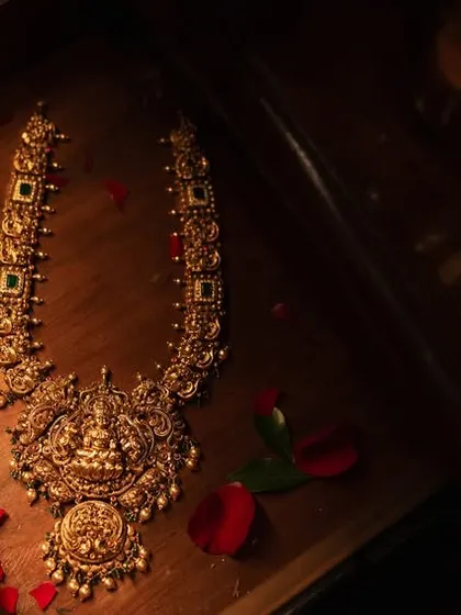 A moody and luxurious flat-lay of the groom's traditional gold jewelry, laid out in a wooden box with rose petals.