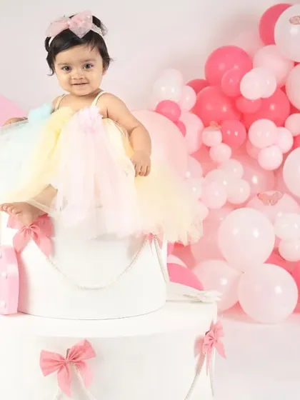 Standing tall like a little queen on her throne. This pose shows off her beautiful dress and the festive balloon arrangement for her first birthday.