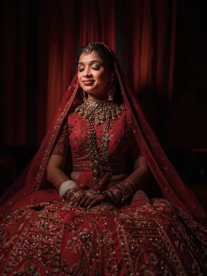 A portrait of the bride in her stunning red lehenga, her eyes closed in a moment of quiet bliss. The rich red tones and soft lighting create a warm and intimate feel.