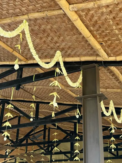 Simple and elegant floral decor using jasmine and palm leaves, hanging from a rustic bamboo ceiling.