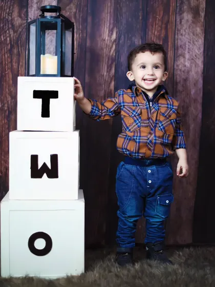 A proud two-year-old stands next to his birthday blocks, smiling for the camera.