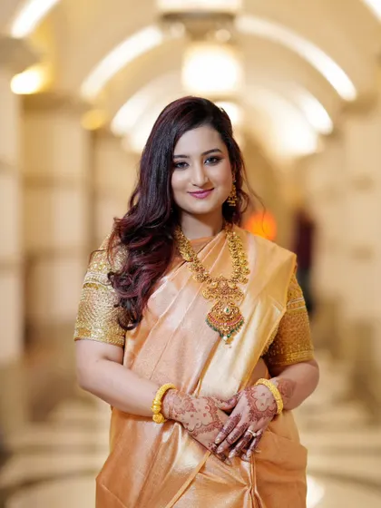 A classic portrait of the bride, with a gentle smile and hands clasped. The focus is on her radiant face and the intricate details of her traditional jewelry.